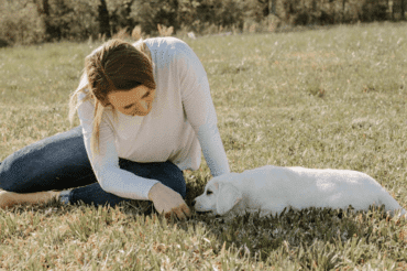 labrador puppy laying on grass next to woman