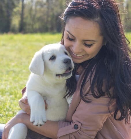 image of woman holding her new white lab puppy and smiling